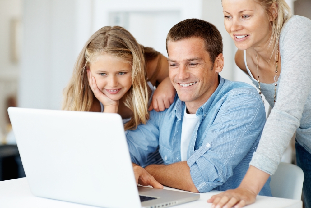 image of husband and wife with their daughter around the kitchen table looking at a computer screen